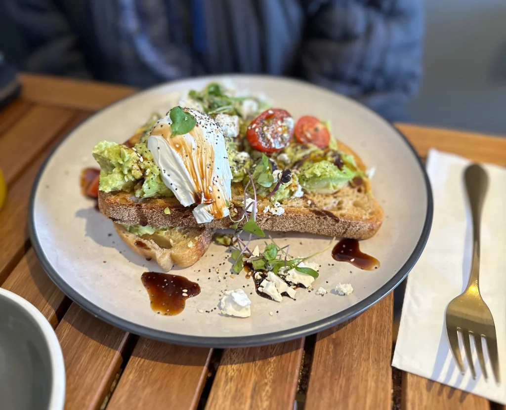 A popular brunch dish of smashed avocado on toast with poached egg, lemon, basil and hummus at Birdcage Café Altona